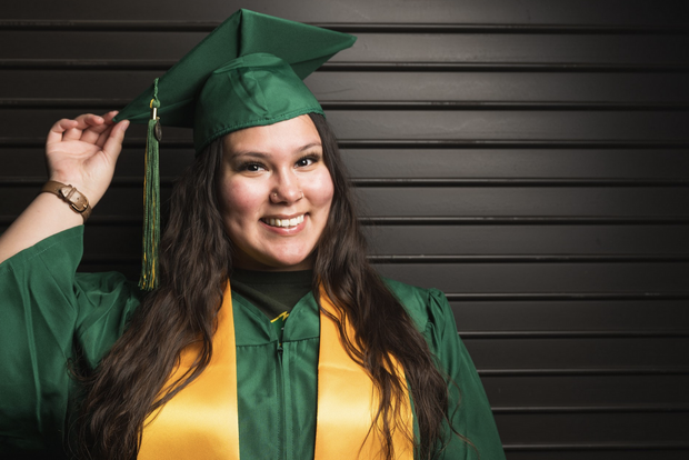 新大毕业生照片, 2023届毕业生, Ambrosia黄鸟, 穿着新大的毕业礼服，戴着绿/黄流苏的学位帽，面带微笑.